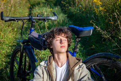 Jovem sentado no chão ao lado de uma bicicleta